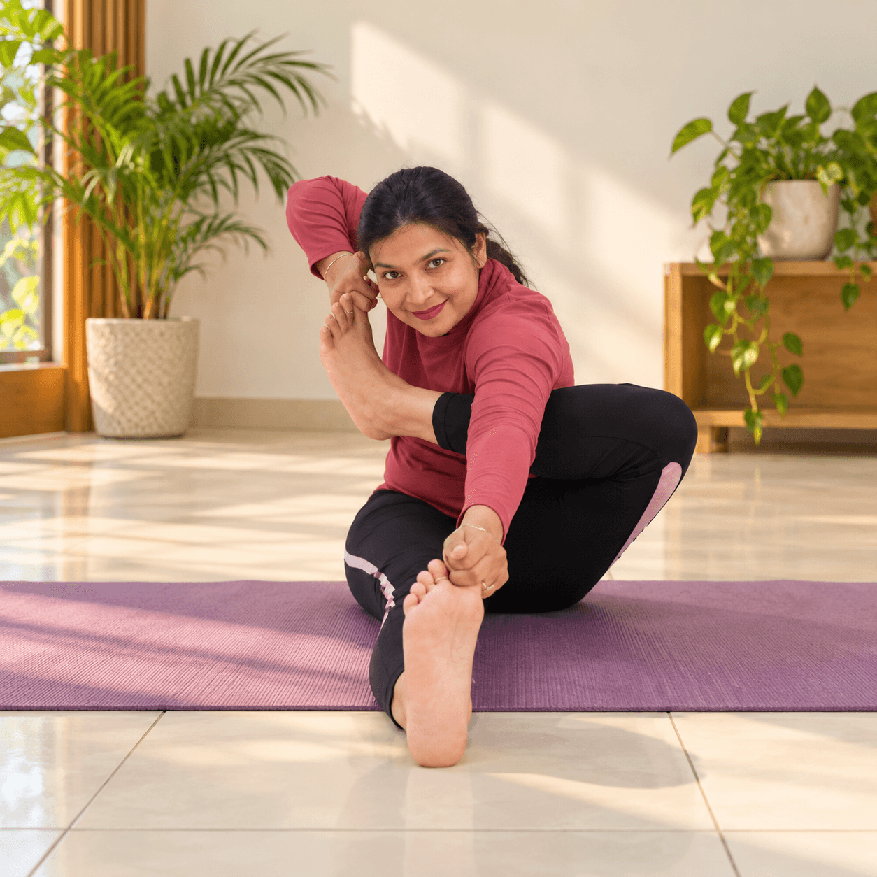 Rajni Kamboj smiling in archer pose on a purple mat, one foot drawn up beside the ear